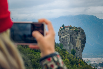 taking photo on mobile device by girl who stay back to camera, rocky dramatic picturesque landscape in Greece, wallpaper travel concept photography with empty copy space for your text