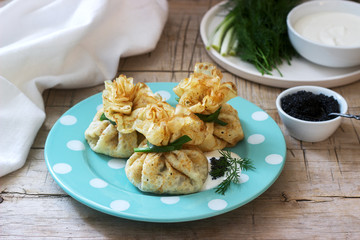 Bags of pancakes stuffed with herring, served with caviar, sour cream and dill on a wooden background. Rustic style.