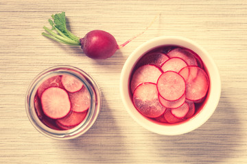 Obraz na płótnie Canvas Fresh radishes cut in thin slices pickled in red wine vinegar with sugar and salt, photographed overhead with natural light (Selective Focus on the top radish slices) (Digitally Altered: Toned Image)