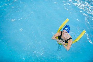 Above view portrait of active senior woman swimming in pool and looking at camera, copy space