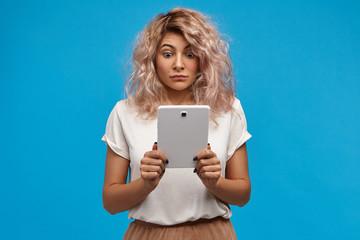 Naklejka premium Funny emotional teenage girl with nose ring and pinkish hair opening eyes wide while staring at screen of digital tablet, being shocked with adult content on internet. Human emotions and gagdets