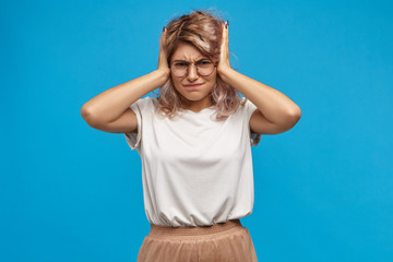 Stop it! Horizontal studio image of frustrated attractive fashionable hipster girl having fight with her jealous boyfriend, can't stand intolerable loud screams, covering her ears, having annoyed look