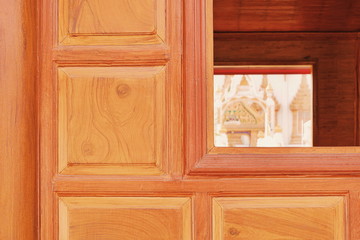 Vintage pattern of teak wooden wall of pavilion with blur part of Thai temple in window frame on traditional Thai architecture design concept, focus on foreground