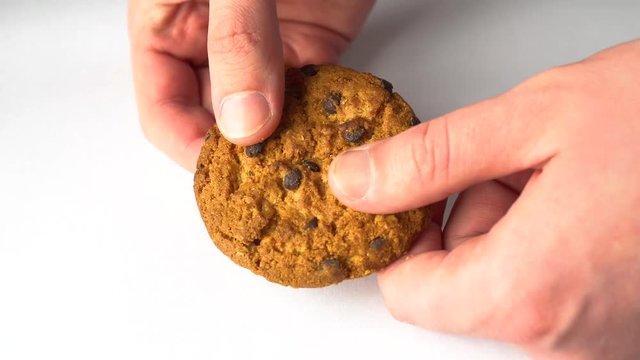 Closeup of a hand grabbing chocolate chip cookie against a white background