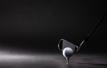 Golf ball, tee and iron on black background
