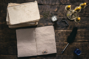 Open blank page book, old literature, pocket watch and a inkwell with quill pen on a writer wooden table background.
