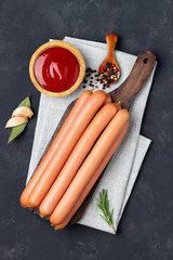 Raw frankfurter sausages with ketchup on cutting board. Top view.