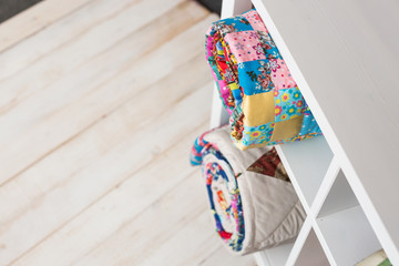 patchwork, sewing and fashion concept - two colorful quilted blankets at white shelves with few storage compartments in studio, white floor in warehouse of finished products, top view.