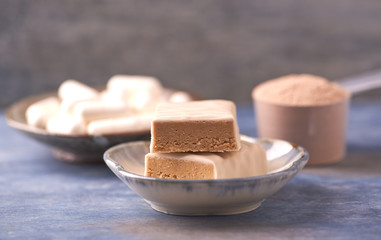 Protein bar in two pieces, creatine capsules and scoop. Bodybuilding food supplements on rustic wooden background. Copy space.