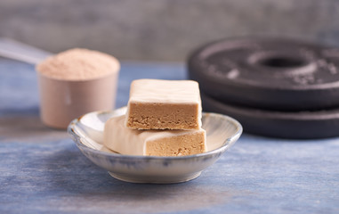 Protein bar in two pieces, scoop and plates.  Nutrition for bodybuilding. Fitness supplements on rustic wooden background. Close up. Copy space