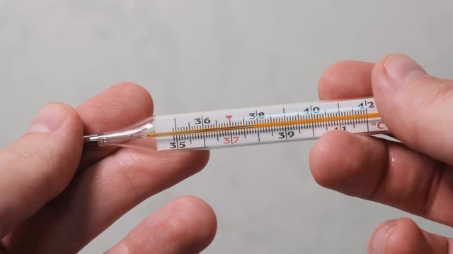 Glass mercurial thermometer takes temperature close up, man hand