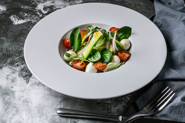 Vegetable salad with avocado, mozzarella, cherry tomatoes and herbs on a large white plate. Instagram toning