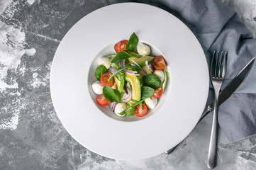 Vegetable salad with avocado, mozzarella, cherry tomatoes and herbs on a large white plate. Instagram toning. Top view