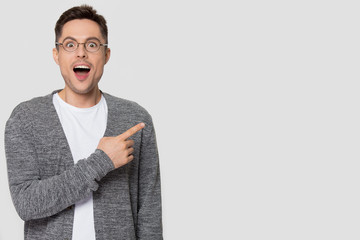 Amazed man in glasses pointing finger aside looking at camera