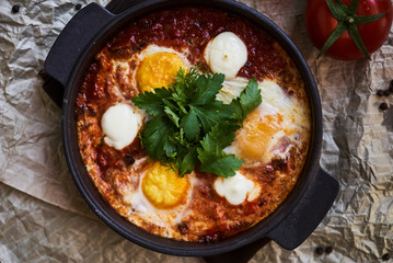 Shakshuka with eggs, tomatoes and parsley in a frying pan, close-up