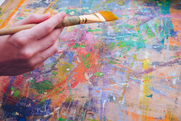 Female artist's hand hold paintbrush and painting a colorful abstract picture with many splatters.