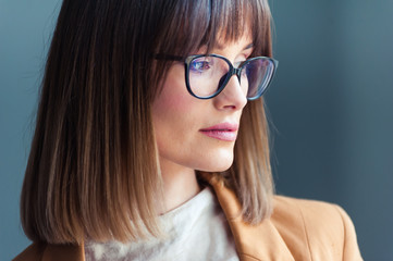 Fototapeta premium Beautiful young woman with glasses, dressed as casual, on a gray background