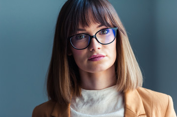 Smiling brunette woman in eyeglasses posing with crossed arms and looking at the camera over grey background