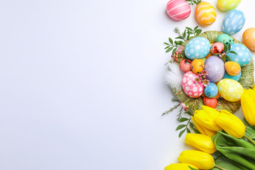 Flat lay composition with nest, Easter eggs, feathers and flowers on color background, space for text