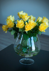 Yellow roses in a glass vase on a black wooden table