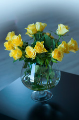 Yellow roses in a glass vase on a black wooden table