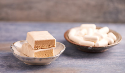 Protein chocolate bar in two pieces and creatine capsules. Bodybuilding food supplements on rustic wooden background. Close up. Copy space.