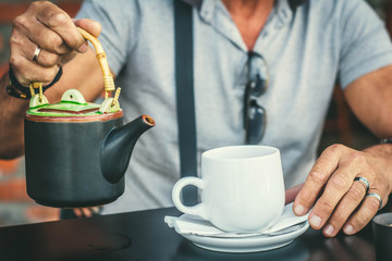 An old man's hands, holding a cup of tea and a teapot