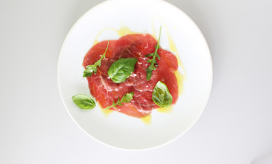 beef carpaccio on a light gray basil background