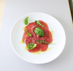 beef carpaccio on a light gray basil background