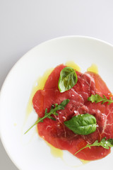 beef carpaccio on a light gray basil background