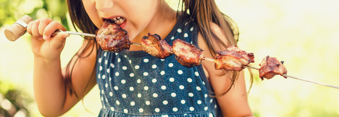 Little girl bites a shish kebab.