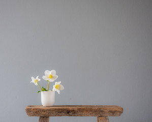 three white flowers in a little ceramic vase on an old wooden stool with lots of copy space