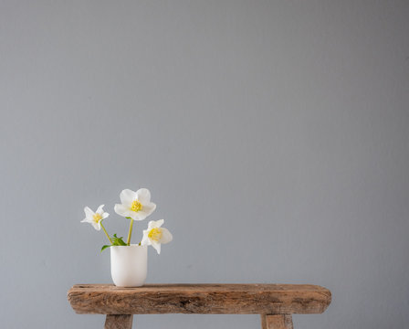 three white flowers in a little ceramic vase on an old wooden stool with lots of copy space