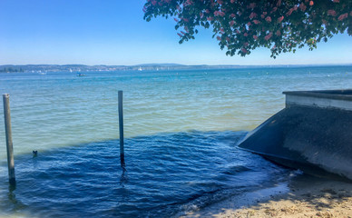 Ufer des Bodensee (Lake of Constance), Schweiz. Bootsteg und grüne Zweige im Vordergrund. Blauer...