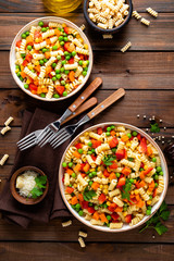 Italian pasta salad with fusilli, corn, boiled carrot, fresh green peas and sweet pepper on wooden rustic background. Top view