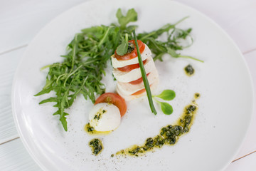 Fresh salad with green rucola, cheese mozzarella, fresh tomatoes on white plate