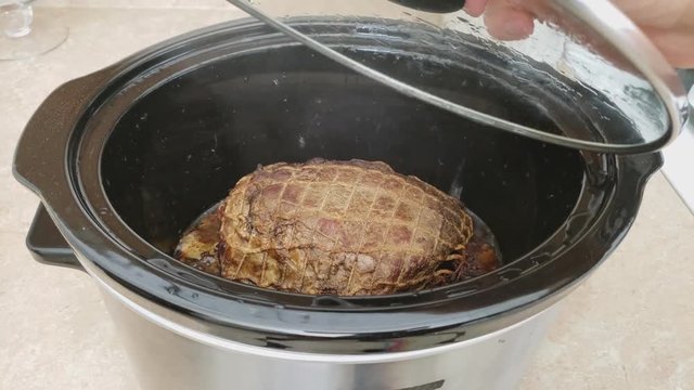 Home cooking - Removing lid from slow cooker exposing almost done previously seared and seasoned Top Sirloin or cut of beef in net bag being cook in low-temperature for about 7 hours.