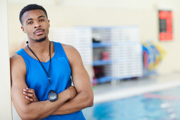 Waist up African-American fitness instructor posing with arms crossed in swimming pool, copy space
