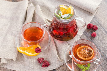 Colorful hot citrus vitamin tea in glass spot and cups