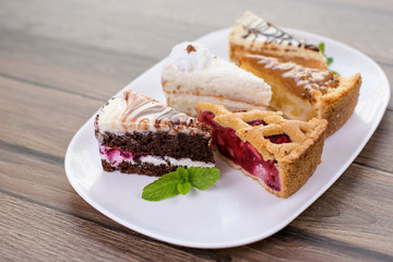 Slices of different delicious cakes on white plate
