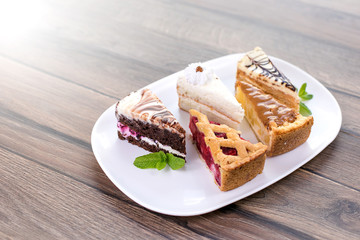Slices of different delicious cakes on white plate