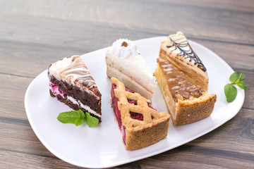 Slices of different delicious cakes on white plate