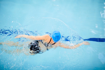 Above view portrait of unrecognizable woman swimming in clear blue water of pool, copy space