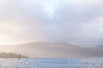 Calm peaceful atmospheric view of lake at Loch Lomond during change of weather from rain to sunshine