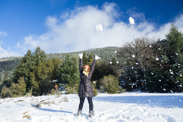 A happy woman throwing snow balls in the air on a snowy mountain