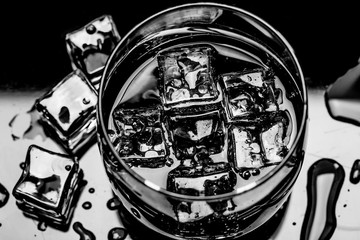 Glass with cola and ice cubes surrounded by ice cubes and water drops.