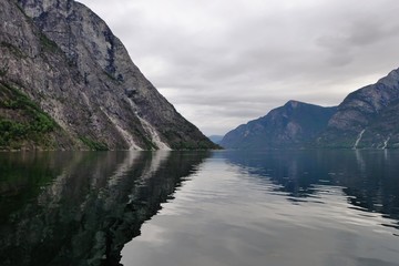 Holy grail illustrated from Sognefjord or Sognefjorden created from mountain range with blue sky and reflection in clear water and having a wooden dock point out in a river in Flåm