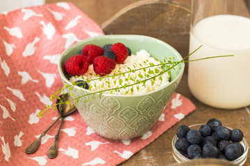 Cottage cheese with fresh raspberries and blueberries in a bowl for a healthy breakfast with ripe berries and milk in a glass bottle.