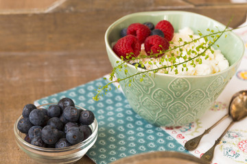 Cottage cheese with fresh raspberries and blueberries in a bowl for healthy breakfast with ripe berries over rustic wooden background.