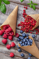Forest fruit berries in ice cream cones with green leaves on wooden table overhead arrangement studio shot